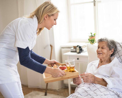 a caregiver serving meal to the senior woman in bed